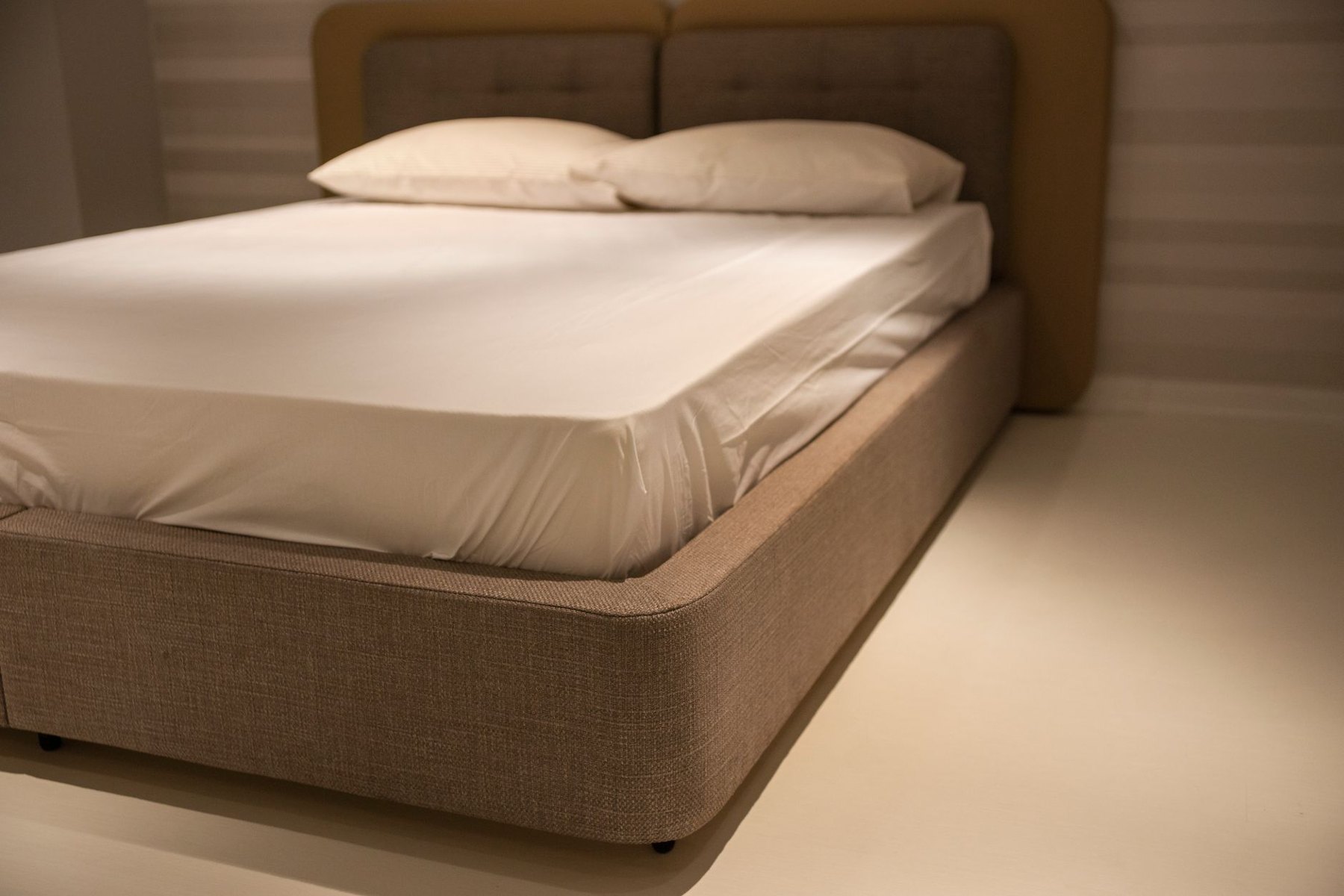Upholstered bed with white bedding and a narrow gap between its base and the floor.