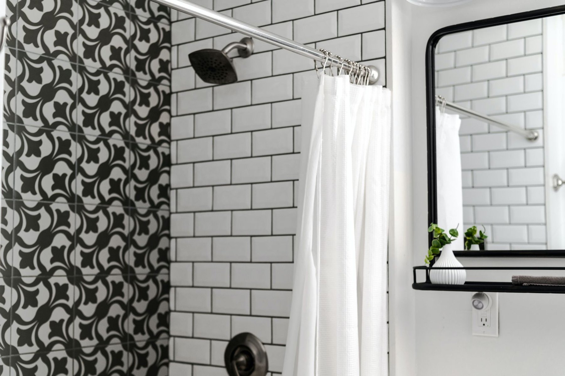 Bathroom with white subway shower tiles, a dark showerhead, a white shower curtain, and a black-framed mirror.
